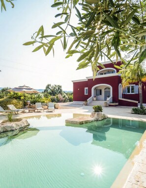 Una villa roja con piscina, mobiliario exterior y vistas del paisaje circundante.