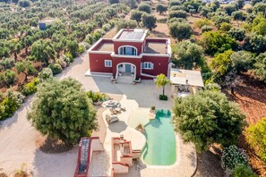 Una casa grande con piscina, rodeada de árboles y un jardín.