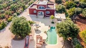 Una casa grande con piscina, rodeada de árboles y un jardín.