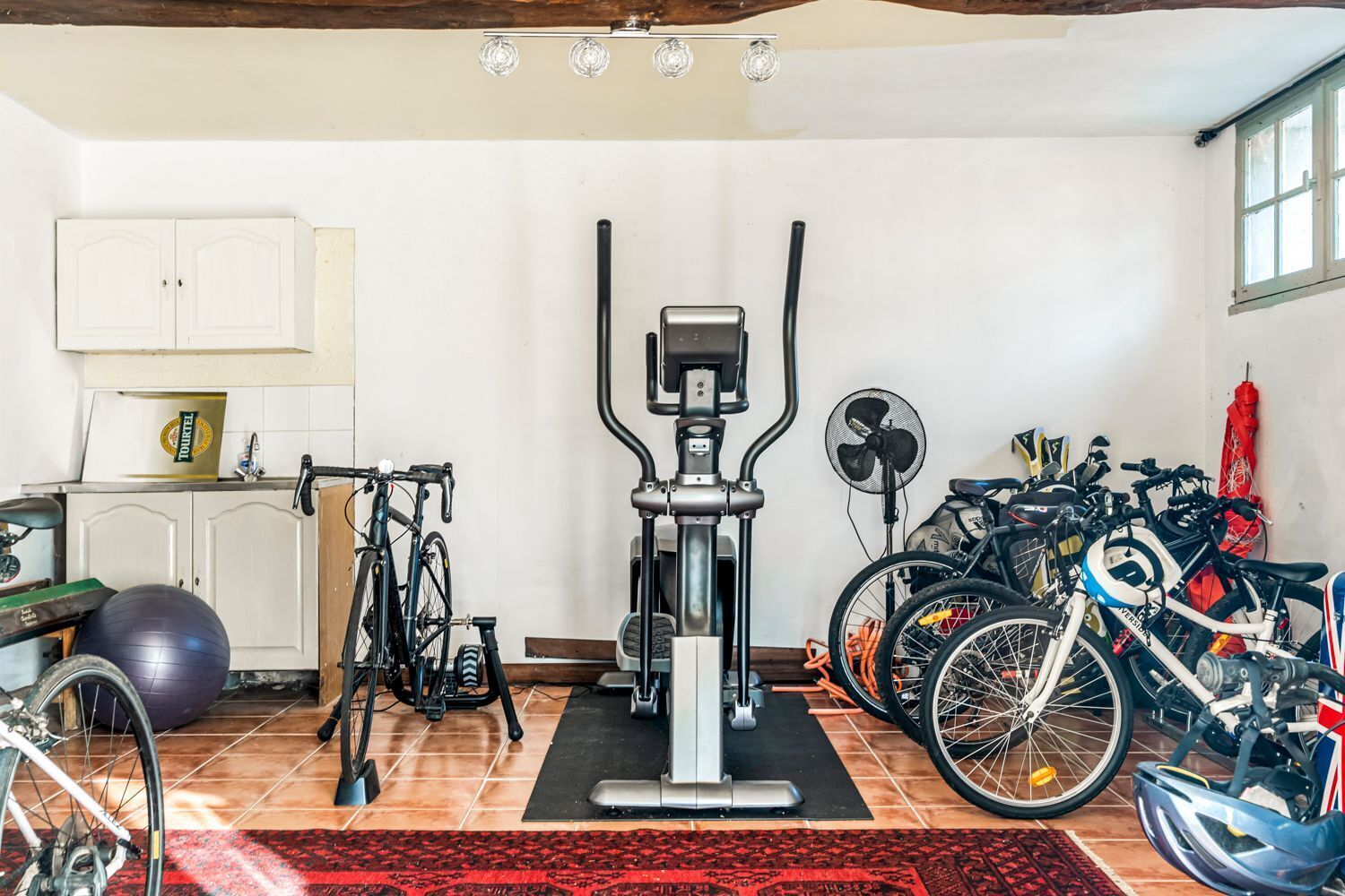 A home gym with exercise equipment, bicycles, and a fan.