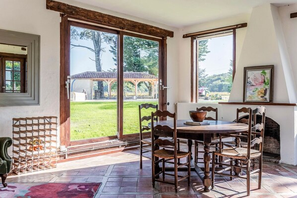 A dining area with a table and chairs, a wooden chair rack, and a view of the garden through a glass door.