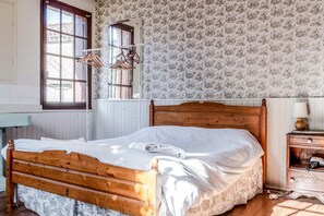Et soveværelse med en træseng, et natbord med en lampe, et spejl og et vindue med tøj hængende.