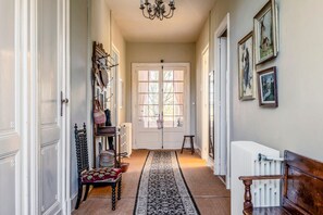 Un pasillo con un radiador, un banco, una silla, una alfombra y una puerta con ventanal.