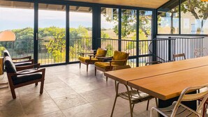 A spacious balcony with a wooden table and chairs, large windows offering a view of greenery and trees. - Le Grand Chene - Five Bedroom Villa, Sleeps 10 (Touffailles)