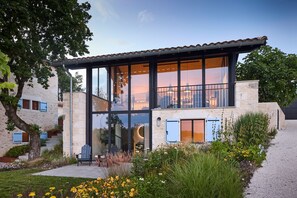 Una casa moderna de dos pisos con grandes ventanales, fachada de piedra y un balcón.