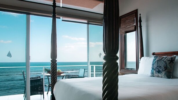 Un lit à baldaquin avec un balcon donnant sur la mer, un coin repas avec une table et des chaises, et une vue sur l’océan.