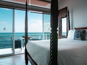 Un lit à baldaquin avec un balcon donnant sur la mer, un coin repas avec une table et des chaises, et une vue sur l’océan.