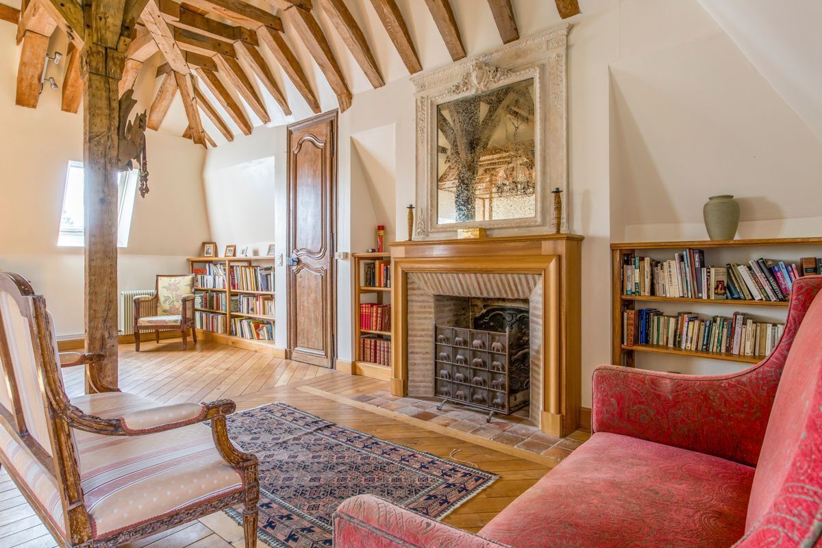 Een gezellige woonkamer met een open haard, boekenkasten en een rode fauteuil.