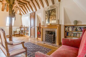 Una sala de estar acogedora con chimenea, estanterías y un sillón rojo.