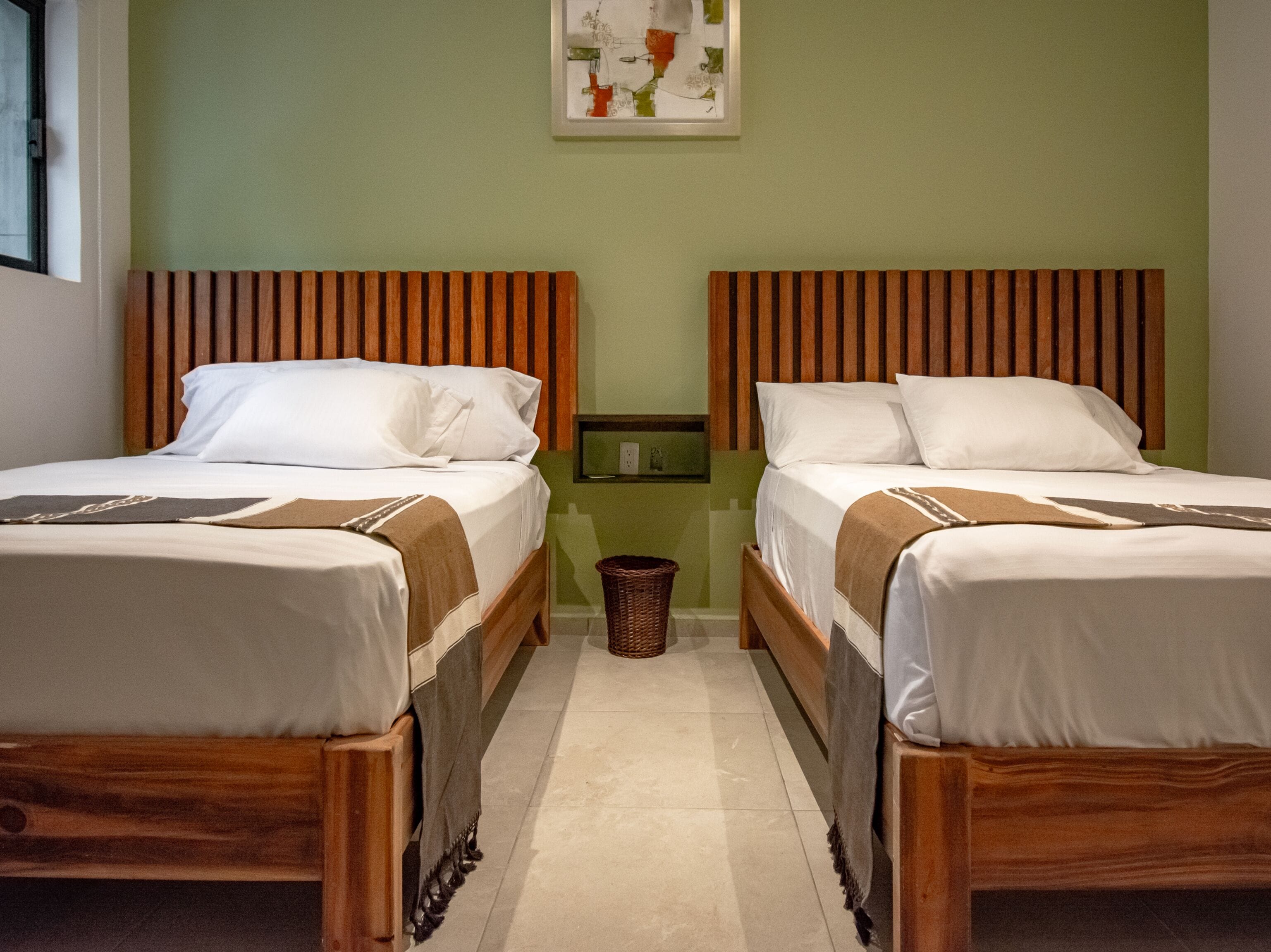 Habitación de hotel con dos camas de madera, una pared verde y una obra enmarcada sobre las camas.