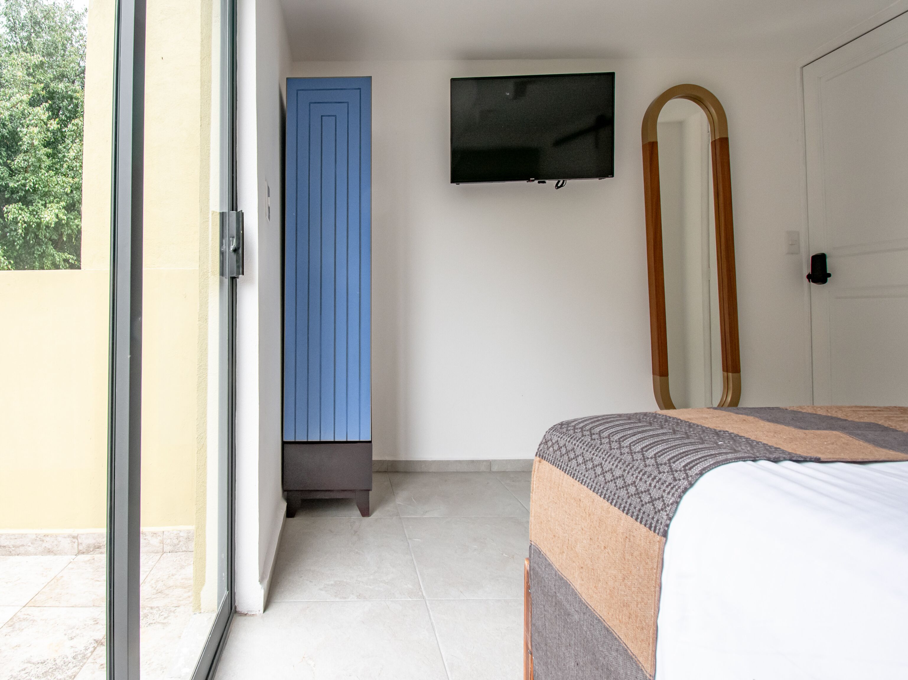 A bedroom with a bed, a television mounted on the wall, and a door.