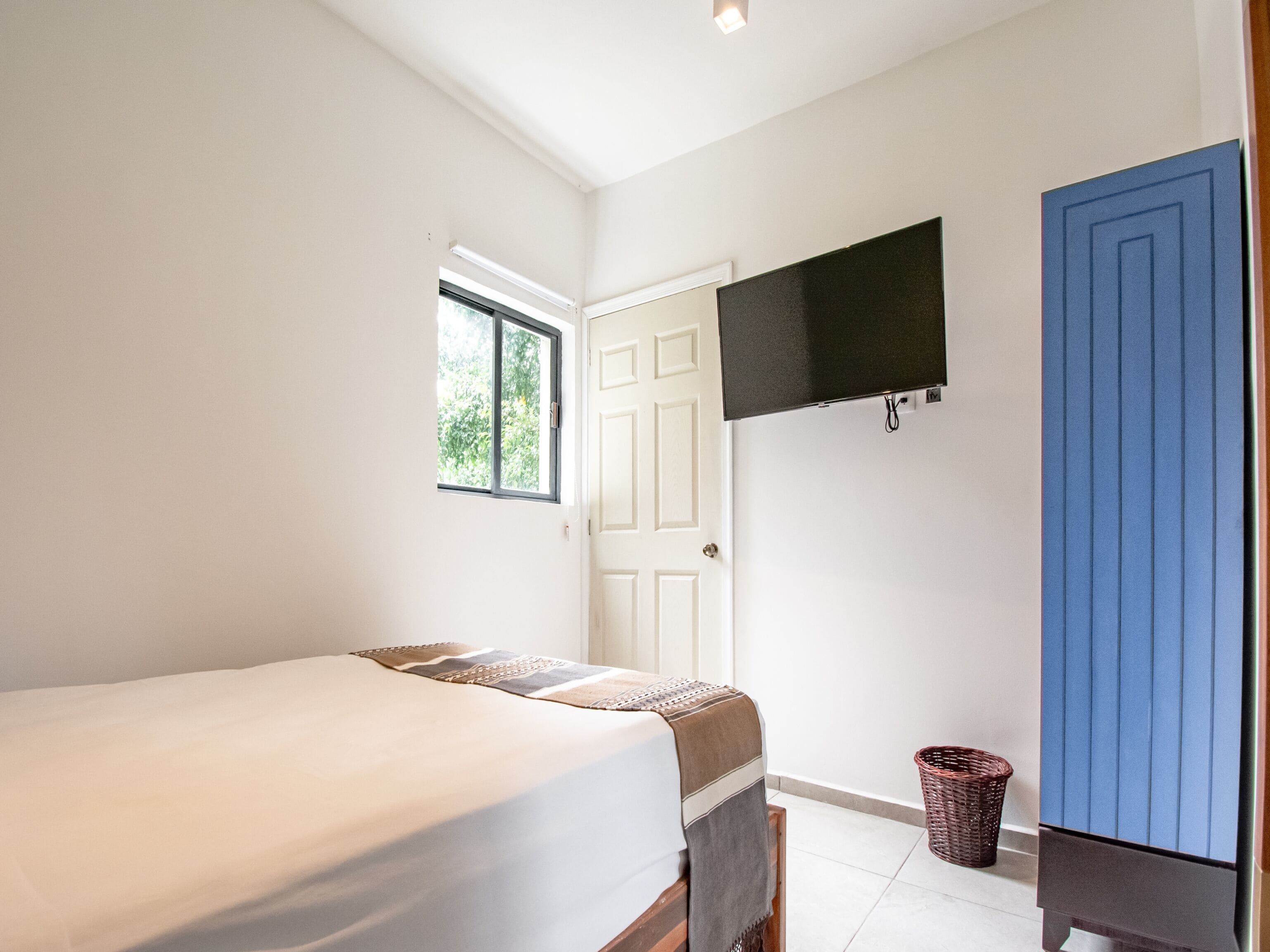 A bedroom with a bed, a TV mounted on the wall, a door, and a window.