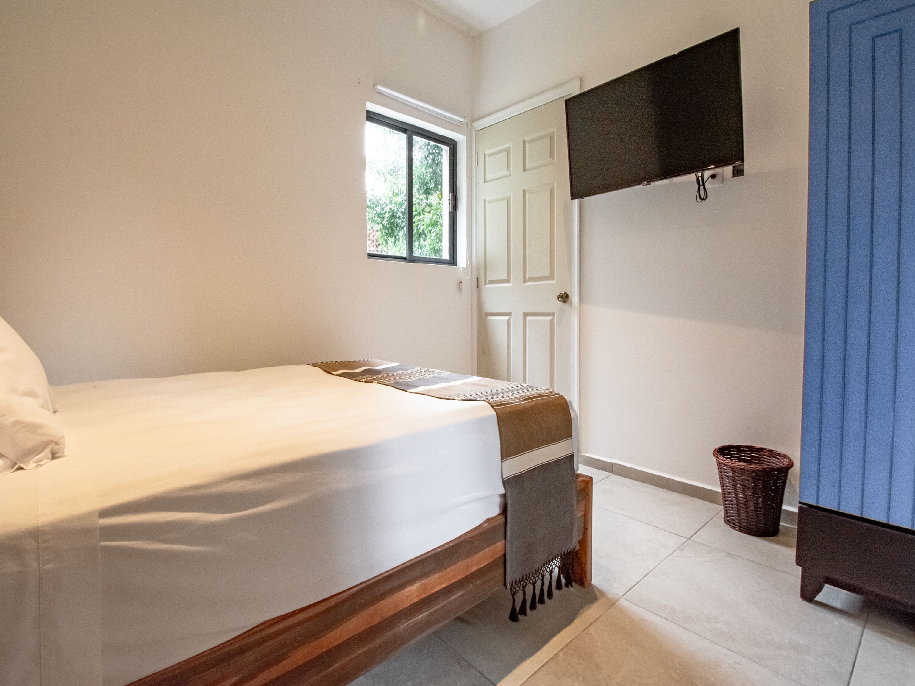 A bedroom with a bed, a window, a door, a television, and a blue cabinet.