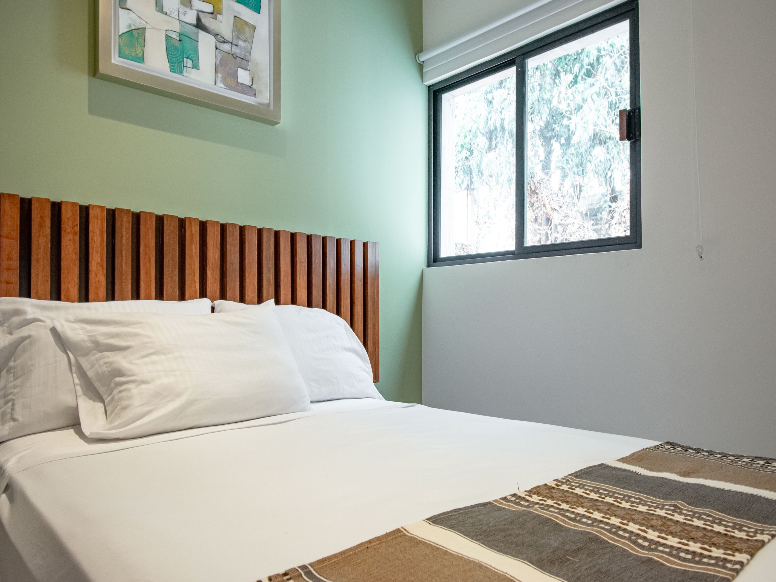 A neatly made bed with white linens, a wooden headboard, and a patterned throw.