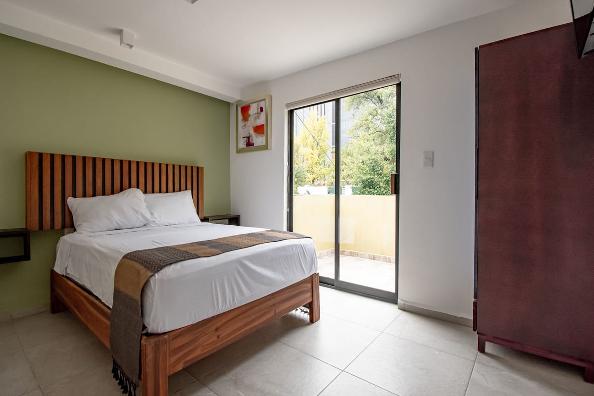 A bedroom with a wooden bed, a green wall, a large window, and a sliding door to a balcony.