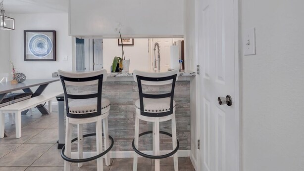 A modern kitchen with white cabinetry, two bar stools, and a dining table.