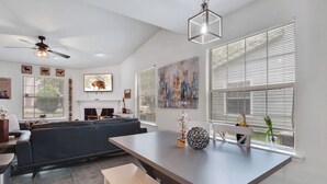A modern living room with a dark sofa, a dining table with a bench, and a ceiling fan.