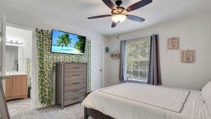 A bedroom with a bed, a ceiling fan, a TV on the wall, and a window with curtains.