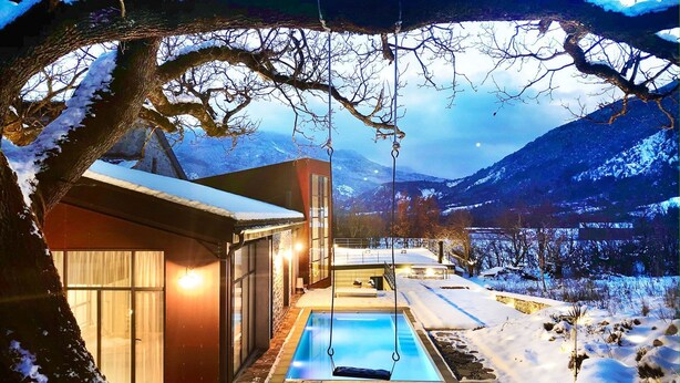 Un bâtiment moderne doté d’une piscine, entouré d’un paysage enneigé et de montagnes.