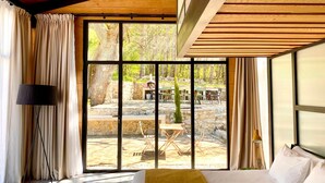 Une chambre avec une grande fenêtre, un lit, une lampe et une vue sur un espace patio extérieur.