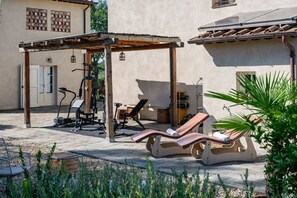 A covered outdoor area with exercise equipment, a lounge chair, and a pergola.