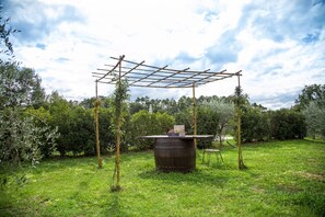 Un jardín con un porche de madera, un barril y una pequeña mesa con una silla debajo.