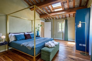 Ein Bett mit Baldachin, mit einem grün gepolsterten Sitzbänkle, Holzboden und einem Oberlicht darüber.