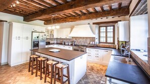 A kitchen with a large island, wooden beams, white cabinets, and a stone floor. - Villa Condotti - Five Bedroom Villa, Sleeps 12 (Montone)