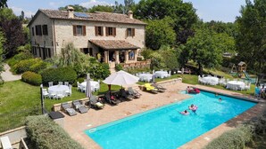 A swimming pool with lounge chairs and umbrellas, surrounded by a garden and a stone building. - Villa Condotti - Five Bedroom Villa, Sleeps 12 (Montone)