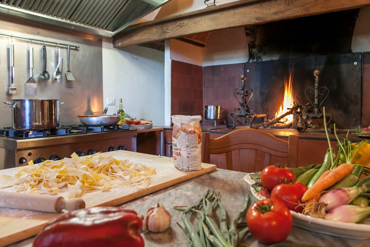 Eine Küche mit Herd, Töpfen, einem Holztisch mit Pasta und frischem Gemüse.