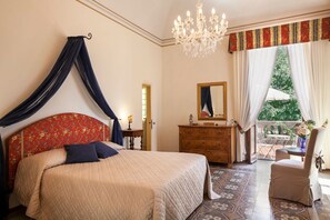 A bedroom with a canopy bed, a chandelier, a dresser, and a view of the outdoors.