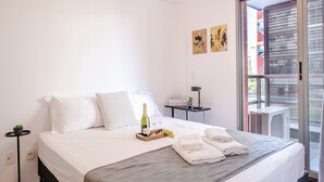 Habitación de hotel con cama, una mesita con botella y vasos, una bandeja con uvas y un balcón con vistas.
