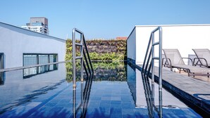 Una piscina infinita con barandillas de metal, cielo despejado y vista de edificios al fondo.