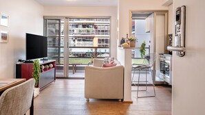 Una sala de estar moderna con televisor de pantalla plana, un sofá, una mesa de comedor y una zona de cocina con refrigerador y horno.