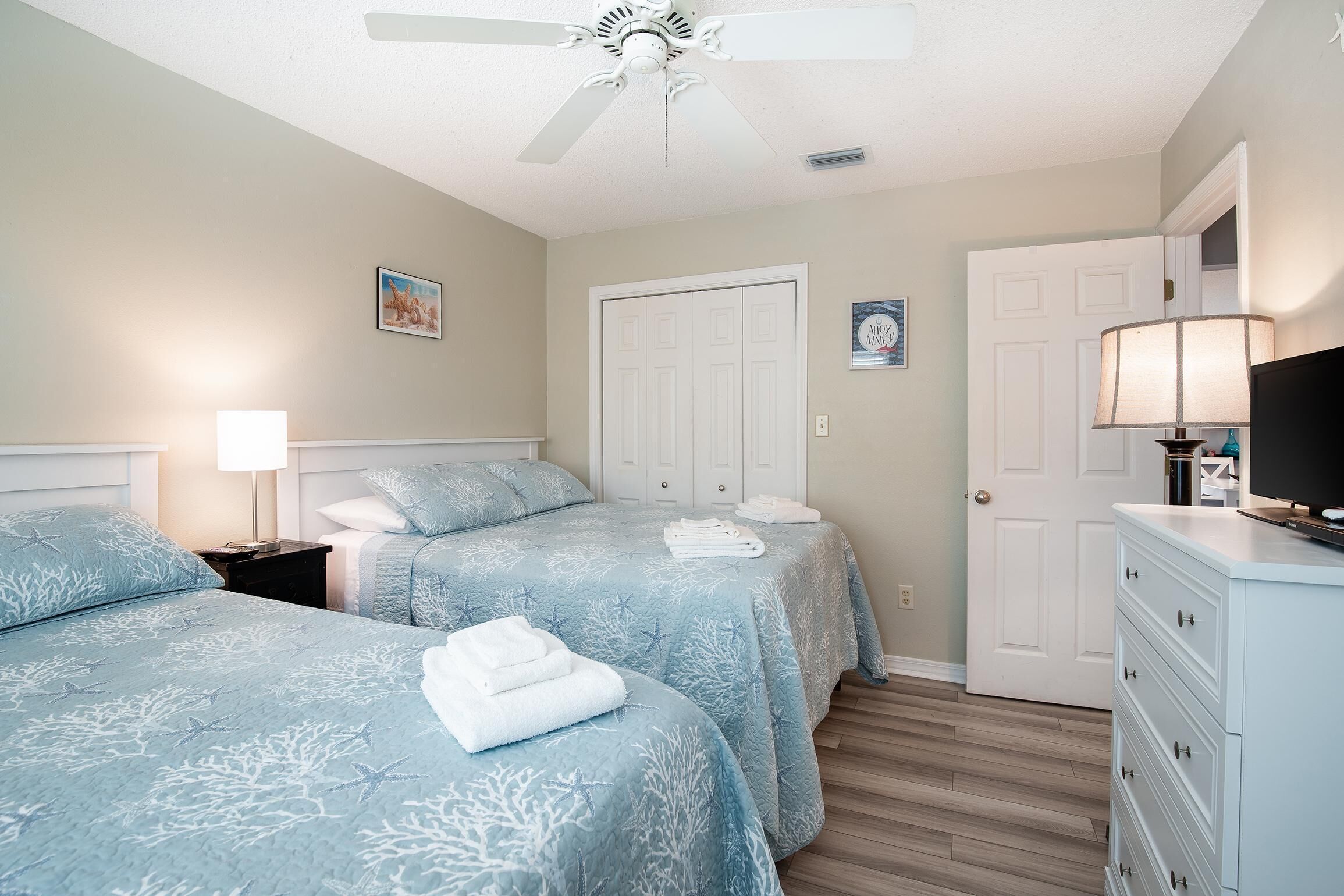 A bedroom with two beds, a ceiling fan, a dresser, and a door.