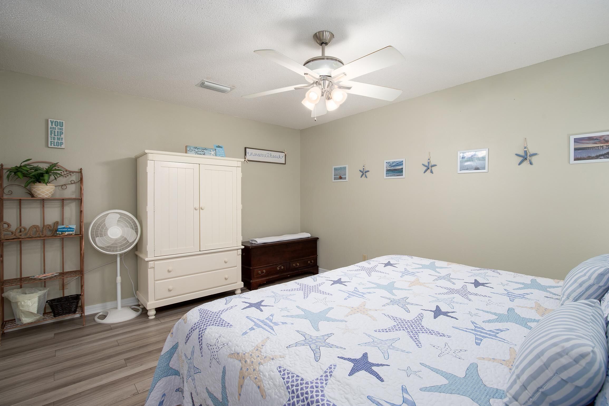 Une chambre à coucher comprenant un lit, un ventilateur de plafond, une commode, une table de chevet et un mur décoré de motifs d’étoiles de mer.