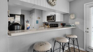 A kitchen with a microwave, a sink, and a counter. There are two stools with numbers on them. - Beachview 107 (Navarre)