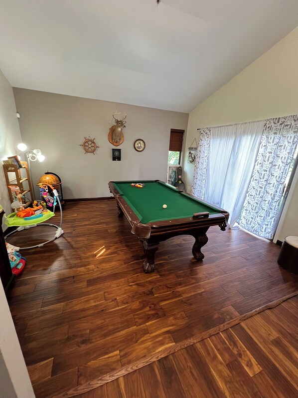 Una mesa de billar en una habitación con suelo de madera, un globo terráqueo, una rueda de barco y una decoración de cabeza de ciervo en la pared.