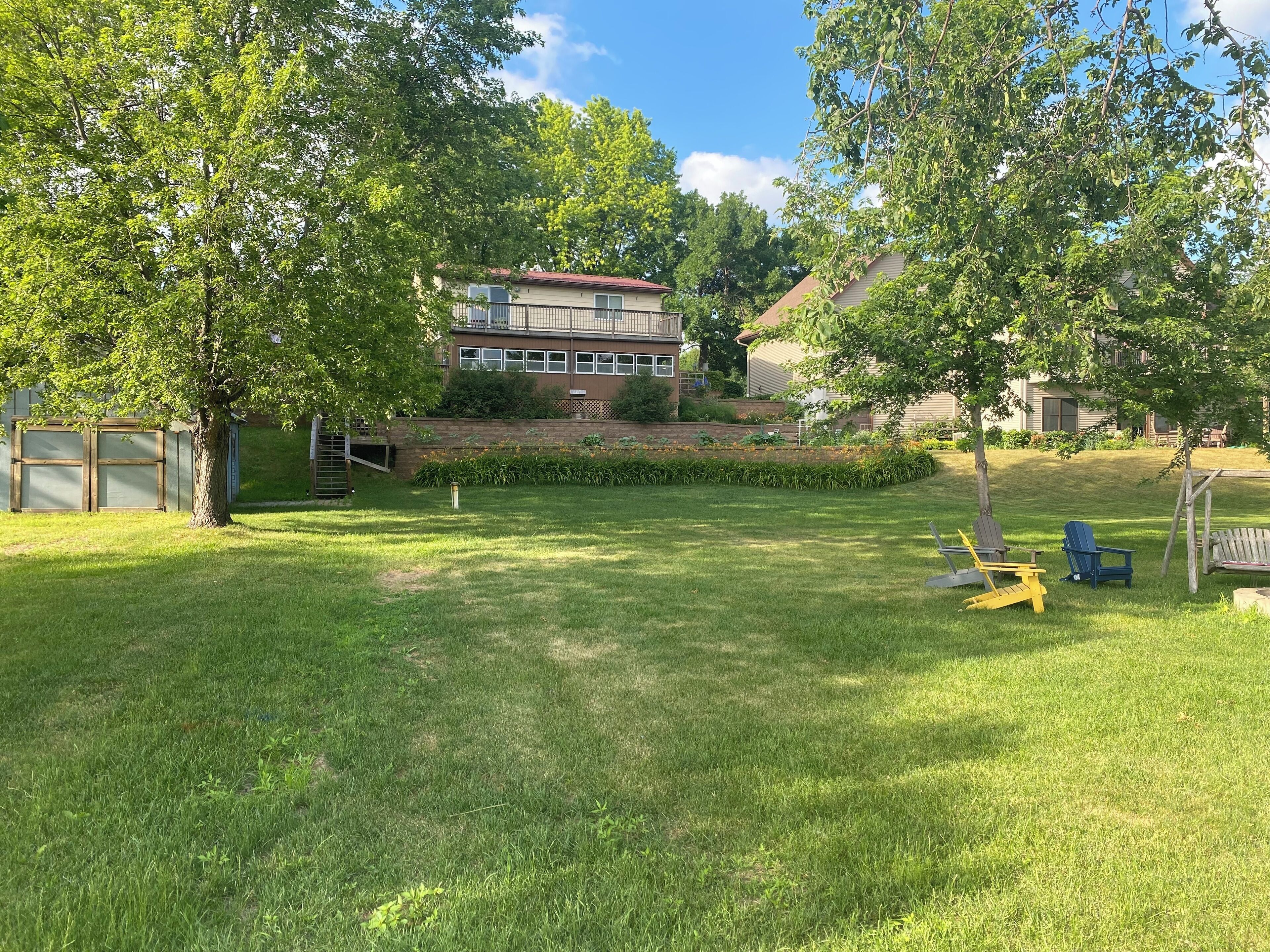 A grassy backyard with a wooden deck, a small garden, and a building in the background.