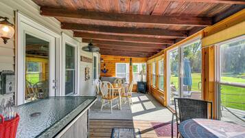A covered outdoor area with a wooden ceiling, a glass-top table, and chairs.
