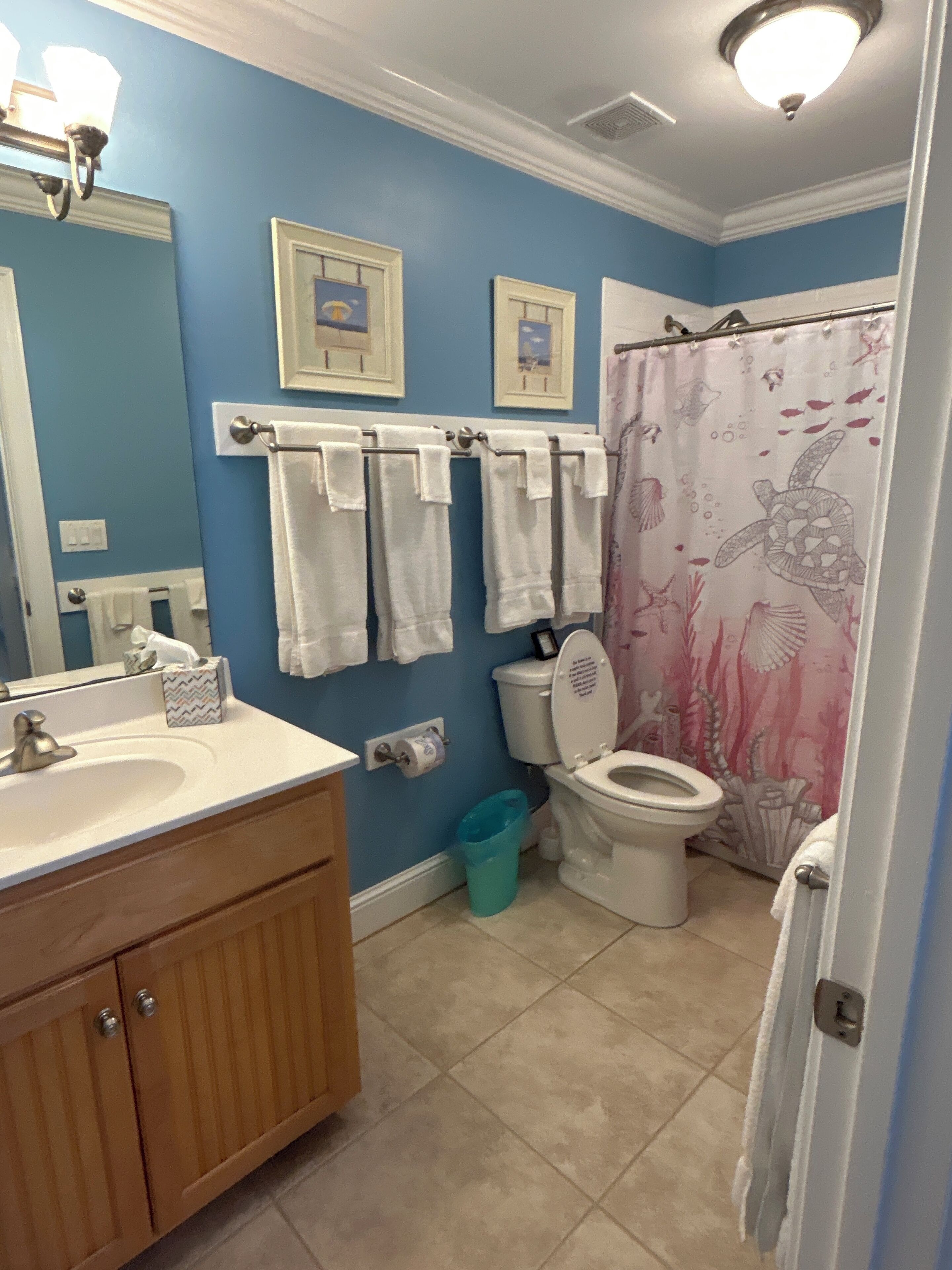 Une salle de bain avec un lavabo, des toilettes et un rideau de douche. Des serviettes sont suspendues sur un porte-serviettes et il y a une poubelle.