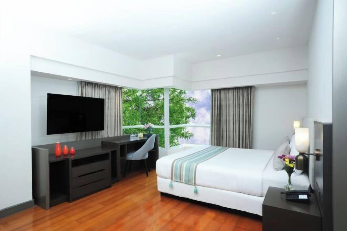 Une chambre d’hôtel moderne dotée d’un grand lit, d’un bureau avec un téléviseur à écran plat et d’une fenêtre donnant sur un paysage verdoyant.