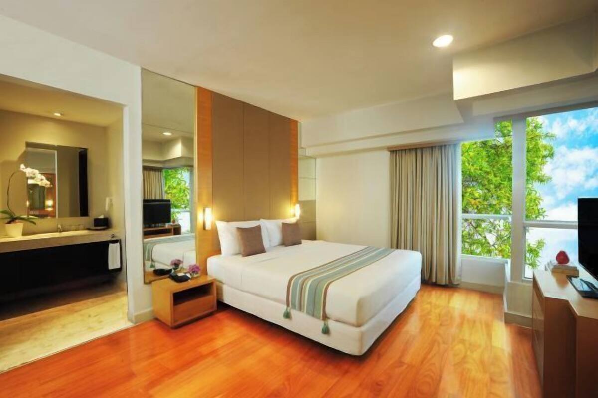 Une chambre d’hôtel équipée d’un lit, d’un bureau, d’une télévision et d’une grande fenêtre donnant sur un beau paysage.