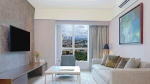 A modern living room with a flat-screen TV, a sofa, a coffee table, and a large window with a city view.