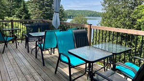 En udendørs terrasse med borde og stole, med udsigt over en sø og et skovområde.