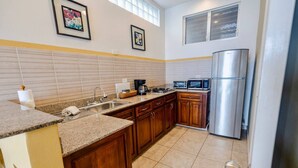A kitchen with wooden cabinets, a stainless steel refrigerator, a microwave, and a coffee maker. - Conch – Oceanfront Ground-Floor Studios – Panama (San Carlos)