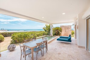 A covered outdoor area with a pool, seating, and a view of the beach. - Apt w 2br-beachfront Private Pool in Sotogrande (Punta Cana)