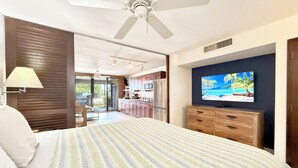 Camera da letto con un letto, una TV, una ventola a soffitto e vista sulla cucina e sul balcone.