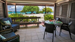Zona relax all'aperto coperta, con mobili in vimini, un tavolo con sottotavola verde e vista sulla spiaggia e l'oceano.