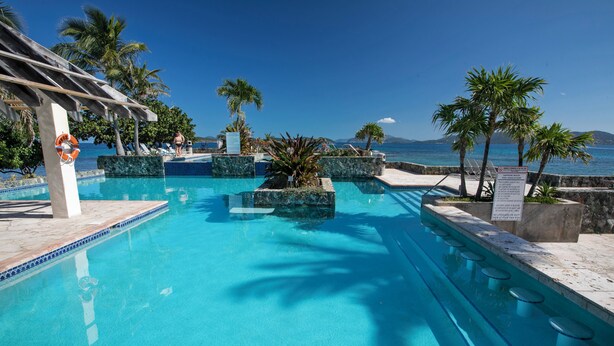 Una piscina cristallina con vista sul mare, circondata da palme e un pergolato.
